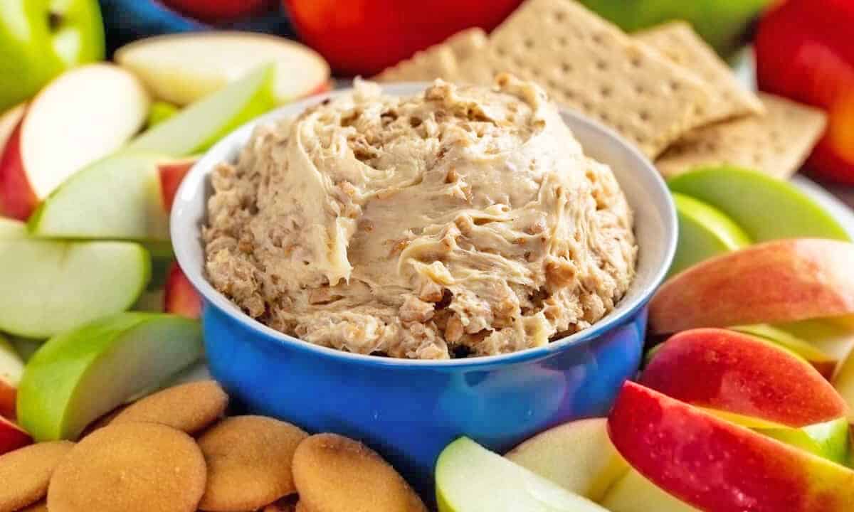 Toffee Apple Dip in a blue bowl surrounded by sliced apples, graham crackers, and Nilla wafers.