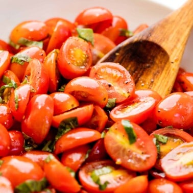 Tomato salad in a white bowl with a wooden spoon in it.