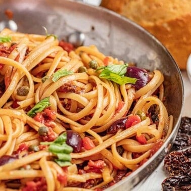 Pasta puttanesca with fresh basil in a skillet.