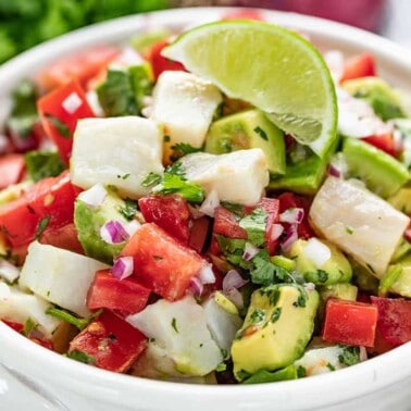 Ceviche topped with a lime wedge in a white bowl.