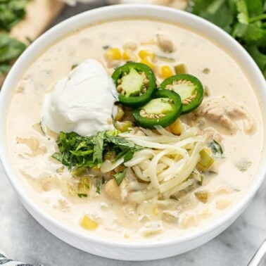 White Chicken Chili topped with cheese jalapeno slices and sourcream all in a white bowl.