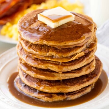 A stack of whole wheat pancakes topped with a pad of butter and syrup.